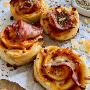 How to Make Sourdough Pizza Rolls | Step by Step Guide 1 Freshly baked sourdough pizza rolls topped with ham, cheese, and herbs on parchment paper
